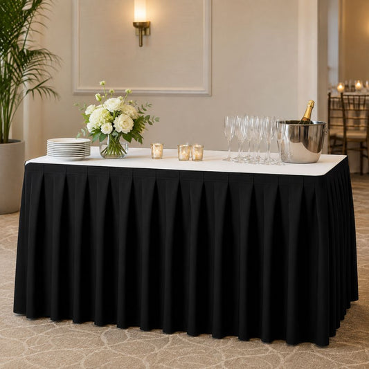 Black pleated table skirt on a rectangular event table with white tabletop, champagne glasses, flowers, candles and serving décor.