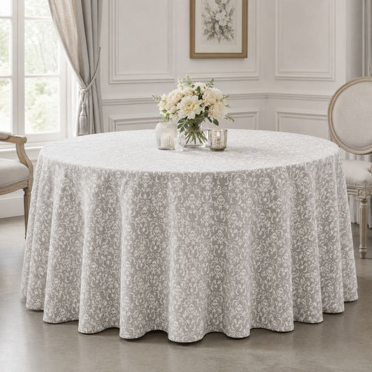 White and grey damask-patterned round tablecloth styled on an elegant table with floral centrepiece and classic neutral décor.