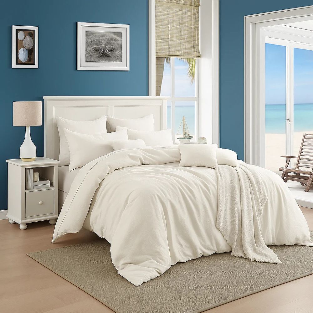 Ivory comforter and layered pillows styled in a bright coastal bedroom with blue walls and seaside-inspired décor.