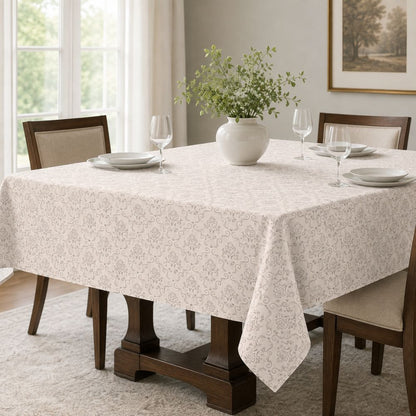 Elegant light beige patterned tablecloth styled on a dining table with white plates, glassware and a ceramic vase centerpiece.