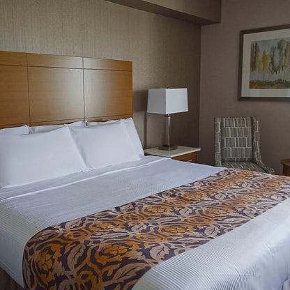 Hotel room with white bed and a bed decorative bedscraf on top with a lamp and chair beside the bed.