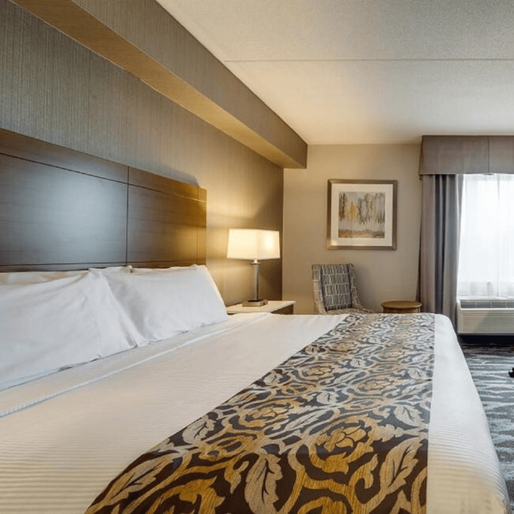 Hotel room with white bed and a bed decorative bedscraf on top with a lamp and chair beside the bed.