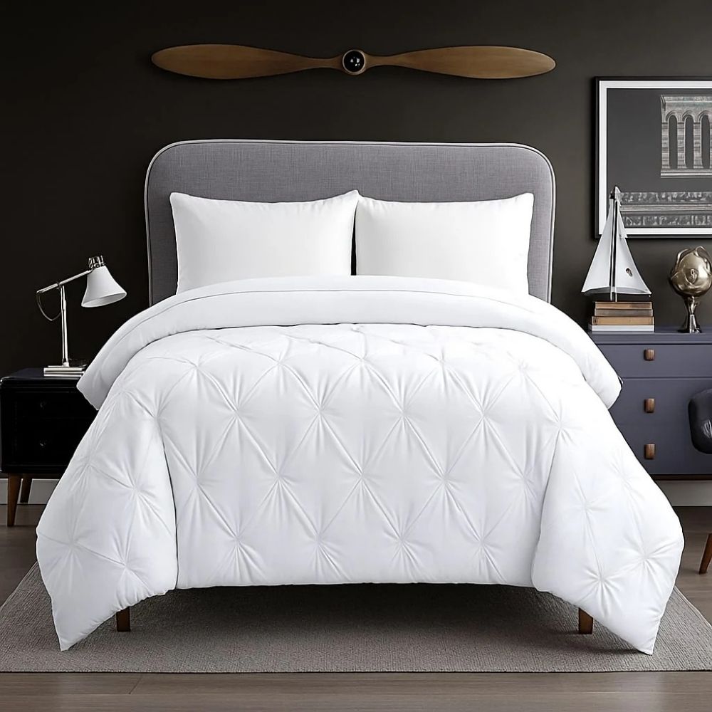 White pinch-pleat comforter styled on a modern bed with crisp white pillows for a clean, bright and luxurious bedroom appearance.