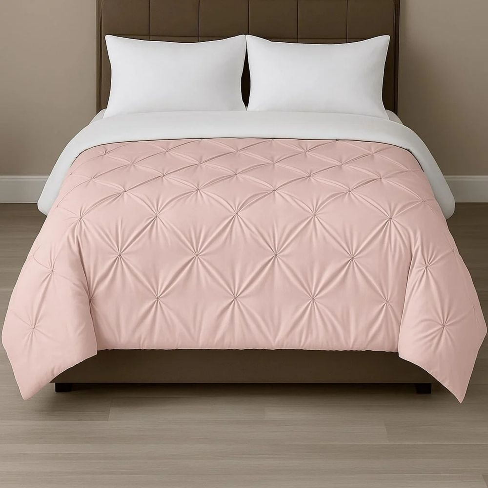 Blush pink pinch-pleat comforter styled on a neatly made bed with crisp white pillows for a soft, elegant bedroom look.