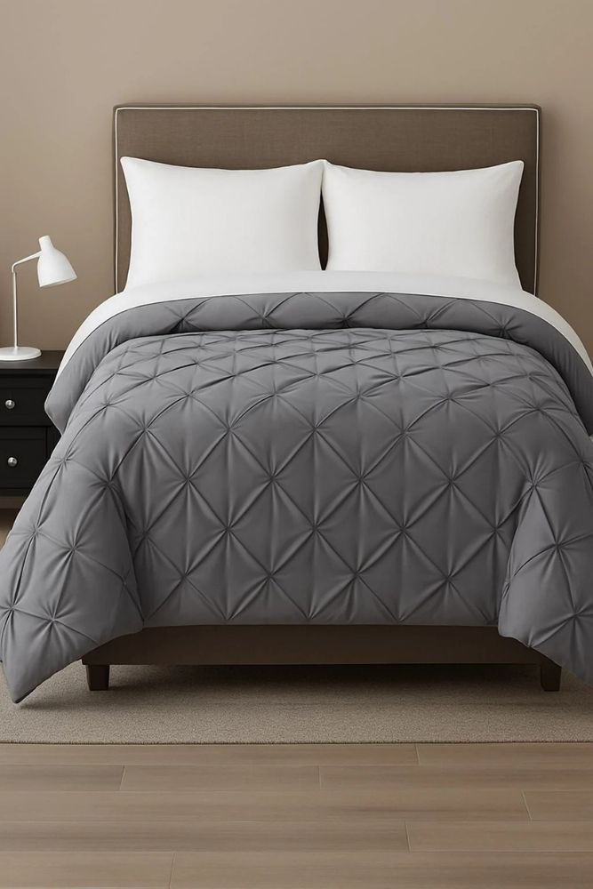 Grey pinch-pleat comforter displayed on a modern bed with white pillows for a refined and contemporary bedroom style.