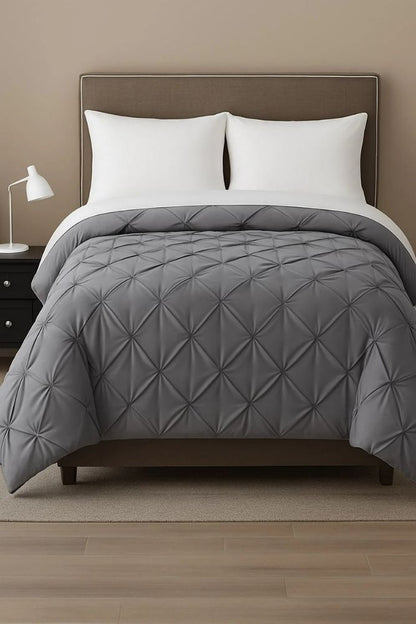 Grey pinch-pleat comforter displayed on a modern bed with white pillows for a refined and contemporary bedroom style.