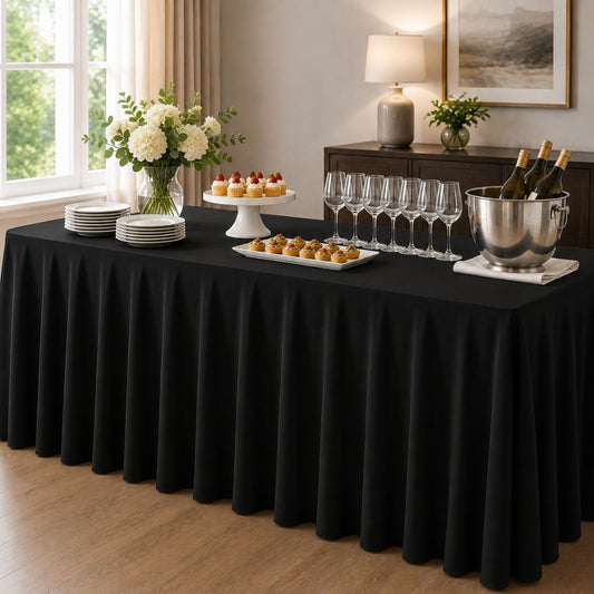 Black pleated tablecloth styled on a rectangular buffet table with plates, desserts, wine glasses, flowers and a beverage cooler for elegant entertaining.