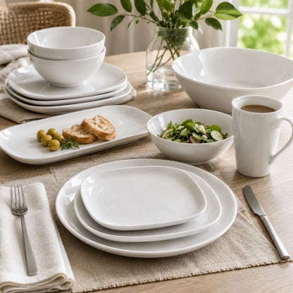 White porcelain dinnerware collection with plates, bowls, mug and serving pieces arranged on a bright modern dining table.