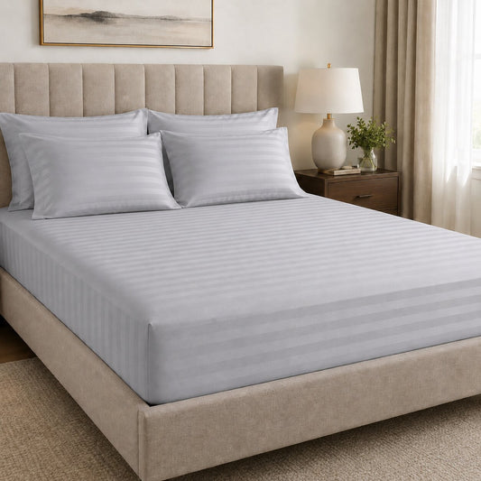 Light grey striped fitted sheet on hotel bed with matching pillowcases for hospitality bedding and linen supply