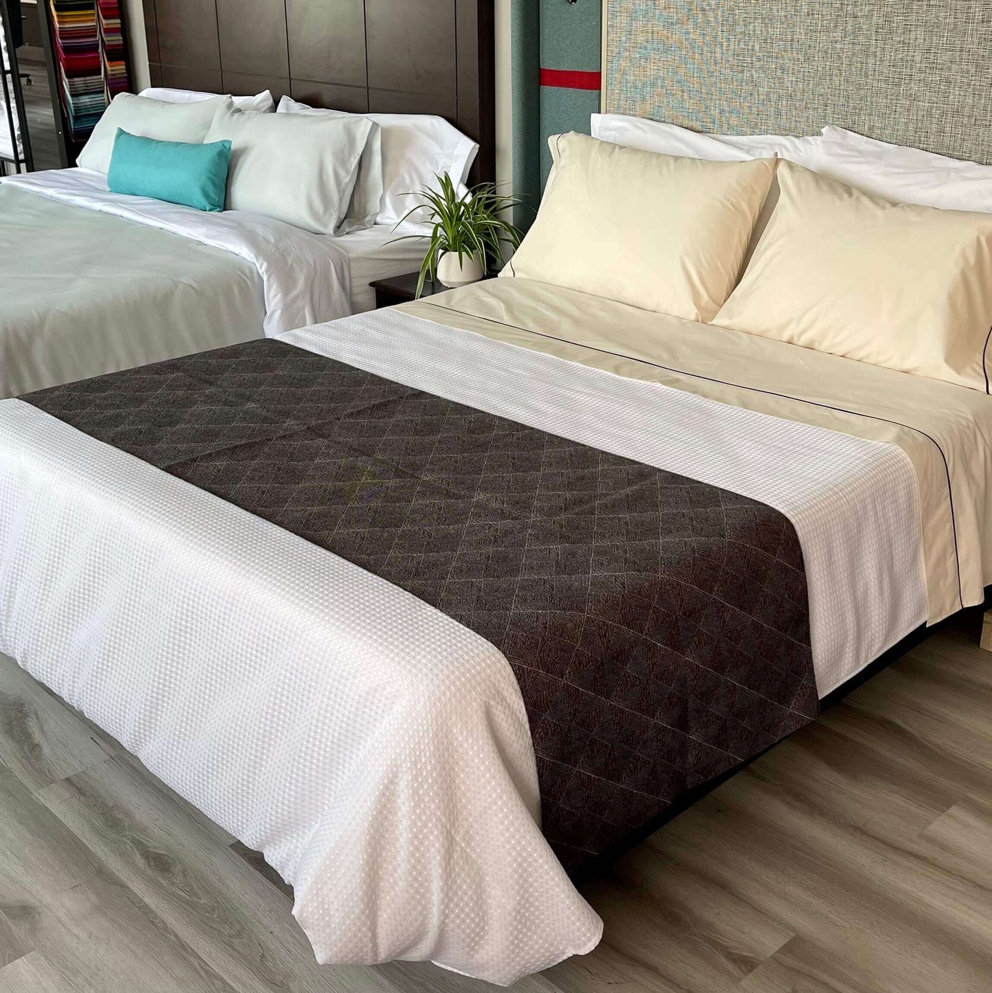 There are two beds next to each other with white bed sheets and decorative pillows near the headboards. The bed that is in close proximity has a bed scarf/ runner in a deep brown colour with white detailing throughout the fabric. 